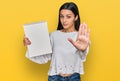 Young hispanic girl holding notebook with open hand doing stop sign with serious and confident expression, defense gesture Royalty Free Stock Photo