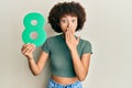 Young hispanic girl holding number eight covering mouth with hand, shocked and afraid for mistake Royalty Free Stock Photo