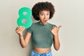 Young hispanic girl holding number eight pointing thumb up to the side smiling happy with open mouth Royalty Free Stock Photo