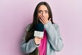 Young hispanic girl holding reporter microphone covering mouth with hand, shocked and afraid for mistake Royalty Free Stock Photo