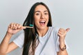 Young hispanic girl holding toothbrush with toothpaste pointing thumb up to the side smiling happy with open mouth