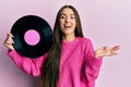 Young hispanic girl holding vinyl disc celebrating achievement with happy smile and winner expression with raised hand Royalty Free Stock Photo