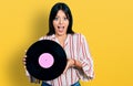 Young hispanic girl holding vinyl disc celebrating crazy and amazed for success with open eyes screaming excited