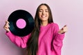 Young hispanic girl holding vinyl disc screaming proud, celebrating victory and success very excited with raised arm