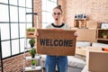 Young hispanic girl holding welcome doormat afraid and shocked with surprise and amazed expression, fear and excited face Royalty Free Stock Photo