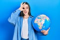 Young hispanic girl holding world ball smiling happy doing ok sign with hand on eye looking through fingers Royalty Free Stock Photo