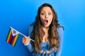 Young hispanic girl holding zimbabwe flag scared and amazed with open mouth for surprise, disbelief face Royalty Free Stock Photo