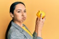 Young hispanic girl looking to piggy bank puffing cheeks with funny face