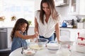 Young Hispanic girl making cake in the kitchen, overseen by her mum, waist up Royalty Free Stock Photo
