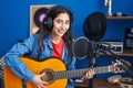 Young hispanic girl musician singing song playing classical guitar at music studio Royalty Free Stock Photo