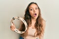 Young hispanic girl playing tambourine scared and amazed with open mouth for surprise, disbelief face Royalty Free Stock Photo