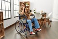 Young hispanic girl sitting on wheelchair at home surprised with hand on head for mistake, remember error