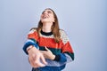 Young hispanic girl standing over blue background laughing at you, pointing finger to the camera with hand over body, shame