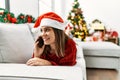 Young hispanic girl talking on the smartphone lying on the sofa by christmas tree at home Royalty Free Stock Photo