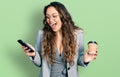 Young hispanic girl using smartphone and drinking a cup of coffee celebrating crazy and amazed for success with open eyes Royalty Free Stock Photo