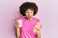 Young hispanic girl using smartphone and drinking a cup of coffee celebrating crazy and amazed for success with open eyes Royalty Free Stock Photo