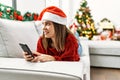 Young hispanic girl using smartphone lying on the sofa by christmas tree at home Royalty Free Stock Photo