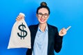 Young hispanic girl wearing business clothes holding dollars bag smiling happy pointing with hand and finger to the side Royalty Free Stock Photo
