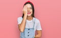 Young hispanic girl wearing casual clothes covering one eye with hand, confident smile on face and surprise emotion Royalty Free Stock Photo