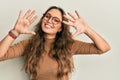 Young hispanic girl wearing casual clothes and glasses showing and pointing up with fingers number ten while smiling confident and