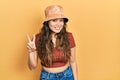 Young hispanic girl wearing casual clothes and hat showing and pointing up with fingers number two while smiling confident and Royalty Free Stock Photo