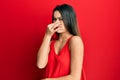 Young hispanic girl wearing casual style with sleeveless shirt smelling something stinky and disgusting, intolerable smell, Royalty Free Stock Photo