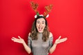 Young hispanic girl wearing deer christmas hat celebrating victory with happy smile and winner expression with raised hands Royalty Free Stock Photo