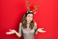 Young hispanic girl wearing deer christmas hat clueless and confused expression with arms and hands raised Royalty Free Stock Photo