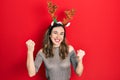Young hispanic girl wearing deer christmas hat screaming proud, celebrating victory and success very excited with raised arms Royalty Free Stock Photo
