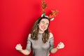 Young hispanic girl wearing deer christmas hat very happy and excited doing winner gesture with arms raised, smiling and screaming Royalty Free Stock Photo