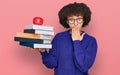 Young hispanic girl wearing glasses holding books and red apple covering mouth with hand, shocked and afraid for mistake Royalty Free Stock Photo