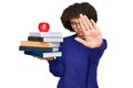 Young hispanic girl wearing glasses holding books and red apple with open hand doing stop sign with serious and confident Royalty Free Stock Photo