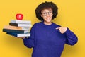 Young hispanic girl wearing glasses holding books and red apple pointing finger to one self smiling happy and proud Royalty Free Stock Photo