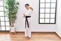 Young hispanic girl wearing karate kimono and black belt smiling looking to the camera showing fingers doing victory sign Royalty Free Stock Photo