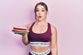 Young hispanic girl wearing sportswear holding carrot cake scared and amazed with open mouth for surprise, disbelief face Royalty Free Stock Photo