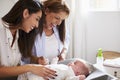 Young Hispanic grandmother and adult daughter playing with her baby son on changing table, close up