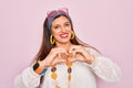 Young hispanic hippie woman wearing fashion boho style and sunglasses over pink background smiling in love showing heart symbol Royalty Free Stock Photo