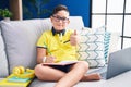 Young hispanic kid doing homework sitting on the sofa approving doing positive gesture with hand, thumbs up smiling and happy for Royalty Free Stock Photo