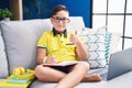 Young hispanic kid doing homework sitting on the sofa doing happy thumbs up gesture with hand Royalty Free Stock Photo