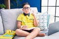 Young hispanic kid doing homework sitting on the sofa pointing up looking sad and upset, indicating direction with fingers, Royalty Free Stock Photo