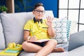 Young hispanic kid doing homework sitting on the sofa waiving saying hello happy and smiling, friendly welcome gesture Royalty Free Stock Photo