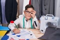 Young hispanic kid at tailor room smiling happy doing ok sign with hand on eye looking through fingers