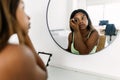 Young hispanic latin woman applying makeup in front of the mirror at bedroom