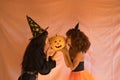 Young Hispanic and Latina women dressed as a witch giving a kiss to a pumpkin on a pink background for Halloween