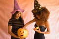 Young Hispanic and Latina women with witch hat reaching into a halloween pumpkin, on pink background Royalty Free Stock Photo