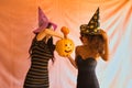 Young Hispanic and Latina women with witch hat reaching into a halloween pumpkin, on pink background