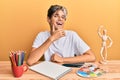 Young hispanic man artist sitting at the studio smiling looking confident at the camera with crossed arms and hand on chin Royalty Free Stock Photo