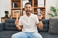 Young hispanic man with beard holding hammer and broken smartphone showing cracked screen celebrating crazy and amazed for success