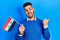 Young hispanic man with beard holding syria flag pointing thumb up to the side smiling happy with open mouth Royalty Free Stock Photo