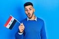 Young hispanic man with beard holding syria flag scared and amazed with open mouth for surprise, disbelief face Royalty Free Stock Photo